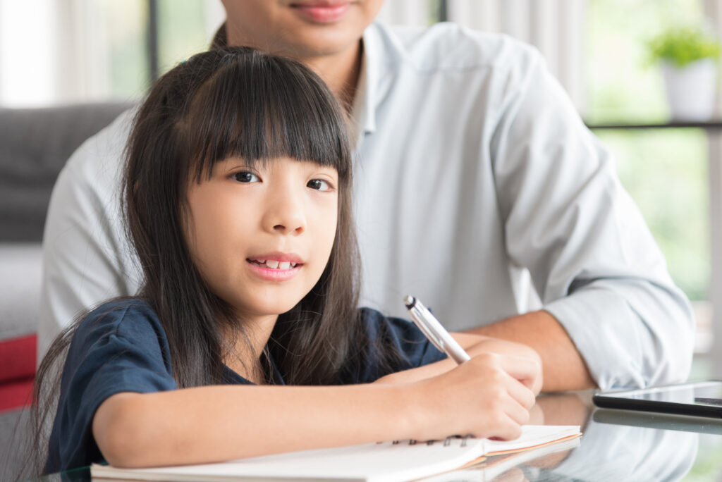 a close up shot of a student at a primary math tuition in Singapore doing her math worksheet while being guided by a tutor