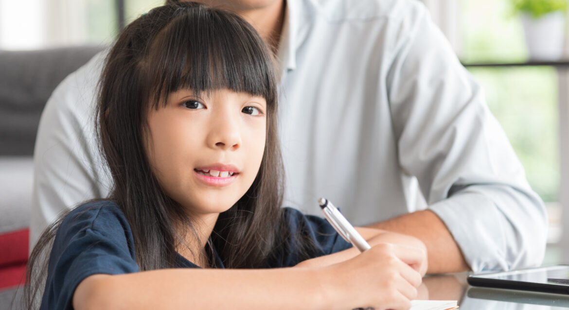A young student with a pen and notebook being tutored on how to solve PSLE problem sums