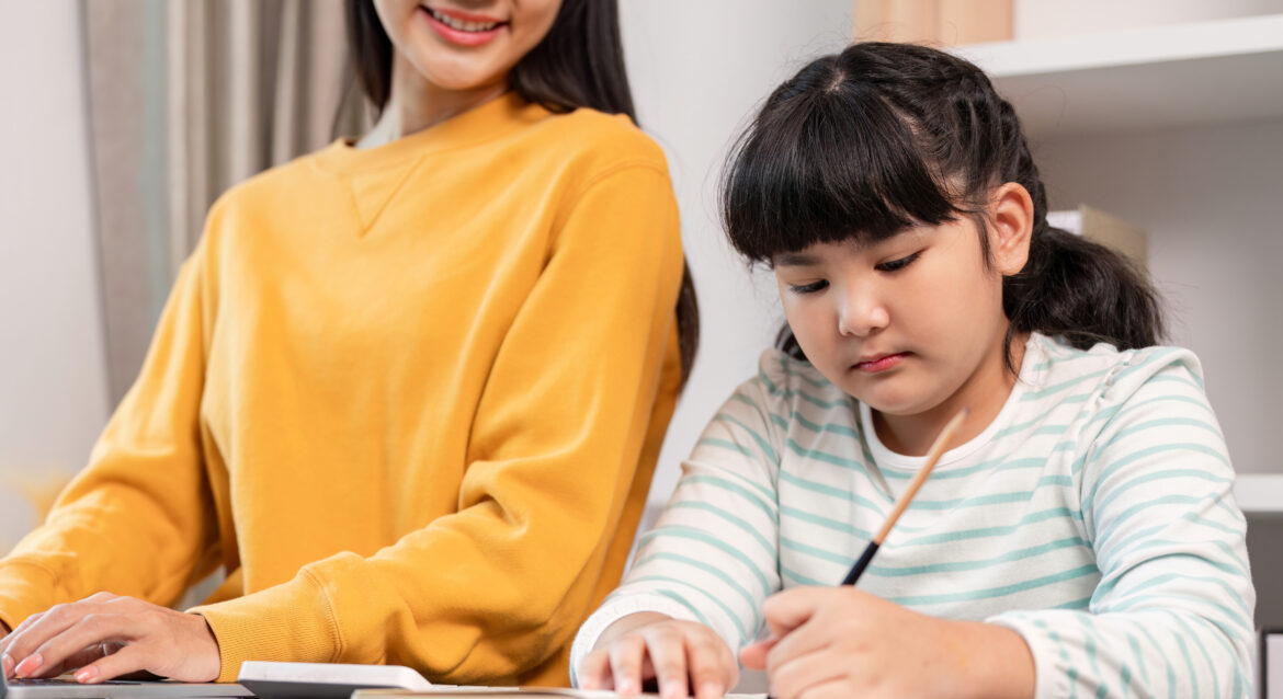 A child working on their math exercises, being coached by her mother on PSLE math tips